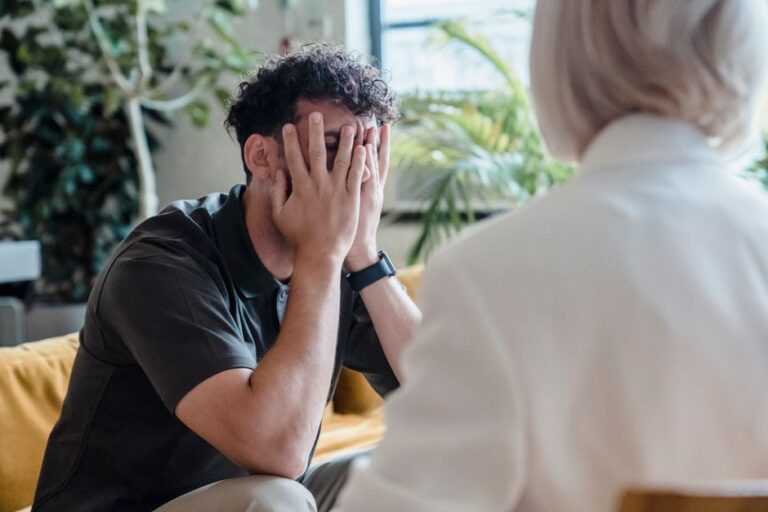 A person quietly observing a group conversation at a community center, holding a notebook and looking thoughtful.