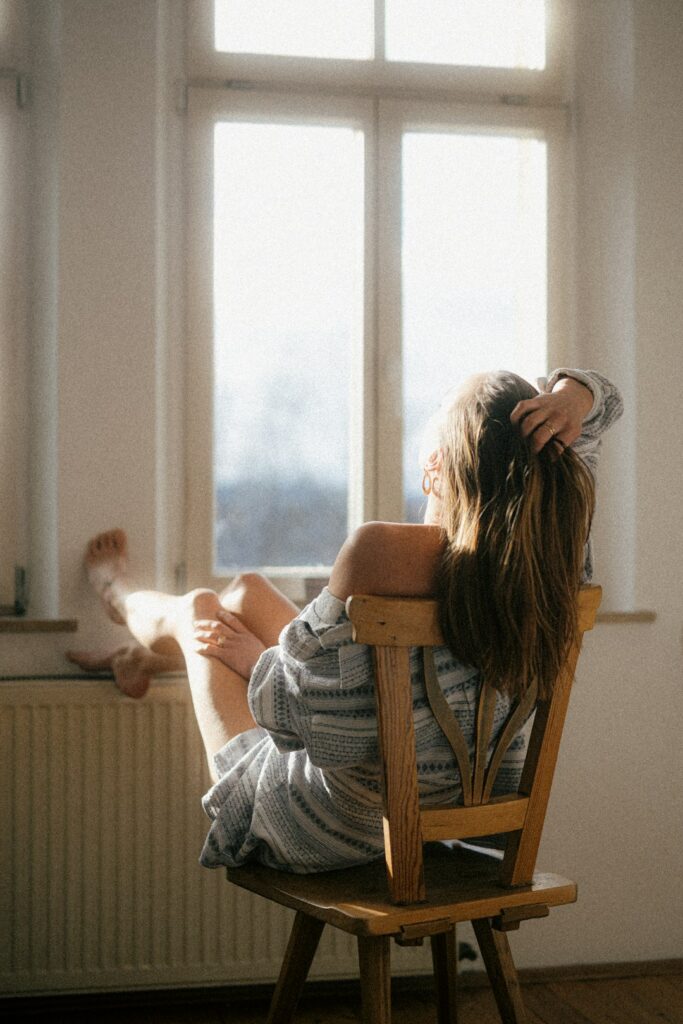 Person sitting by a bright window with a light therapy lamp, journal, and warm blanket.